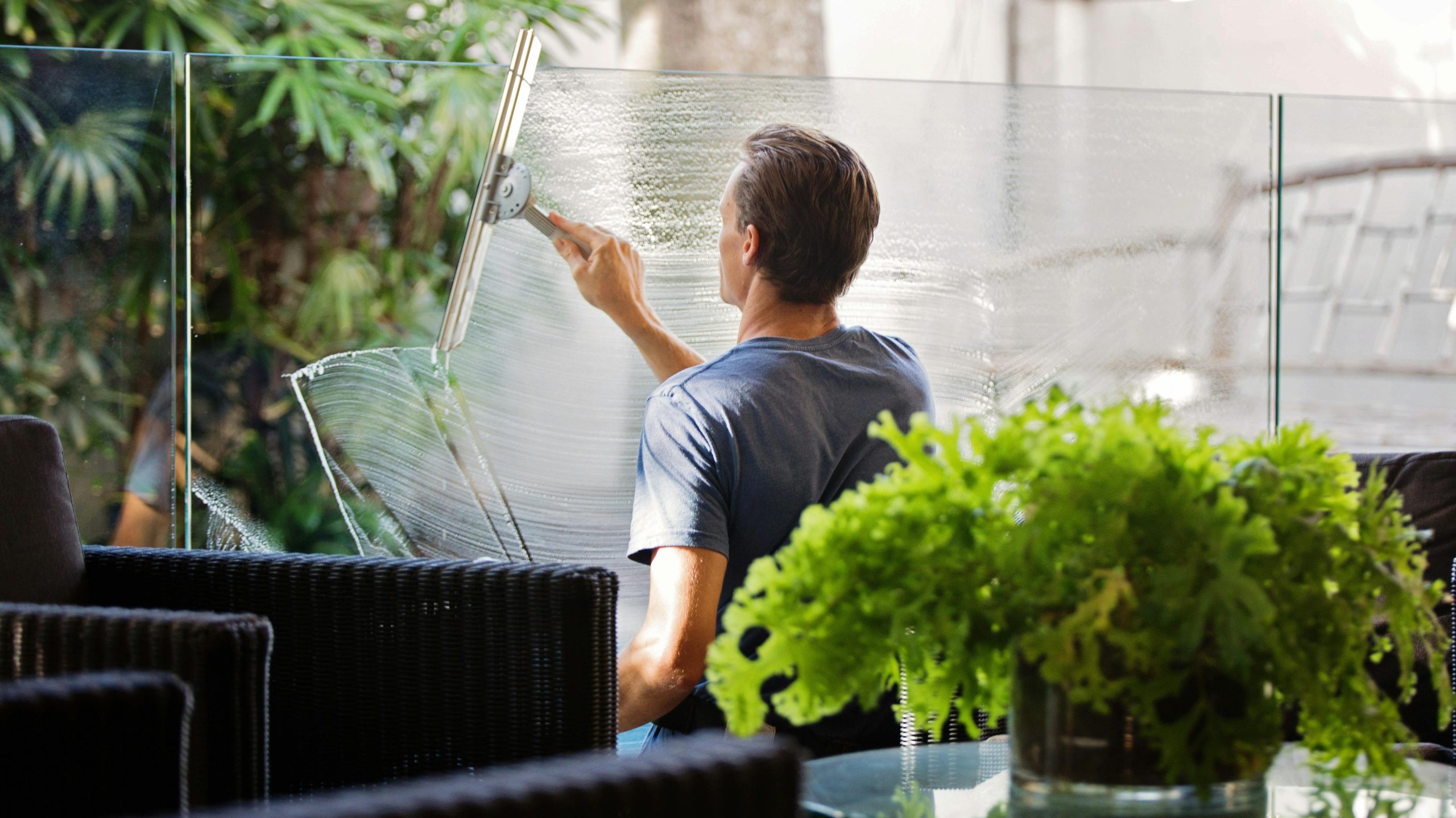 Man in Gray Shirt Cleaning Clear Glass Wall Near Sofa